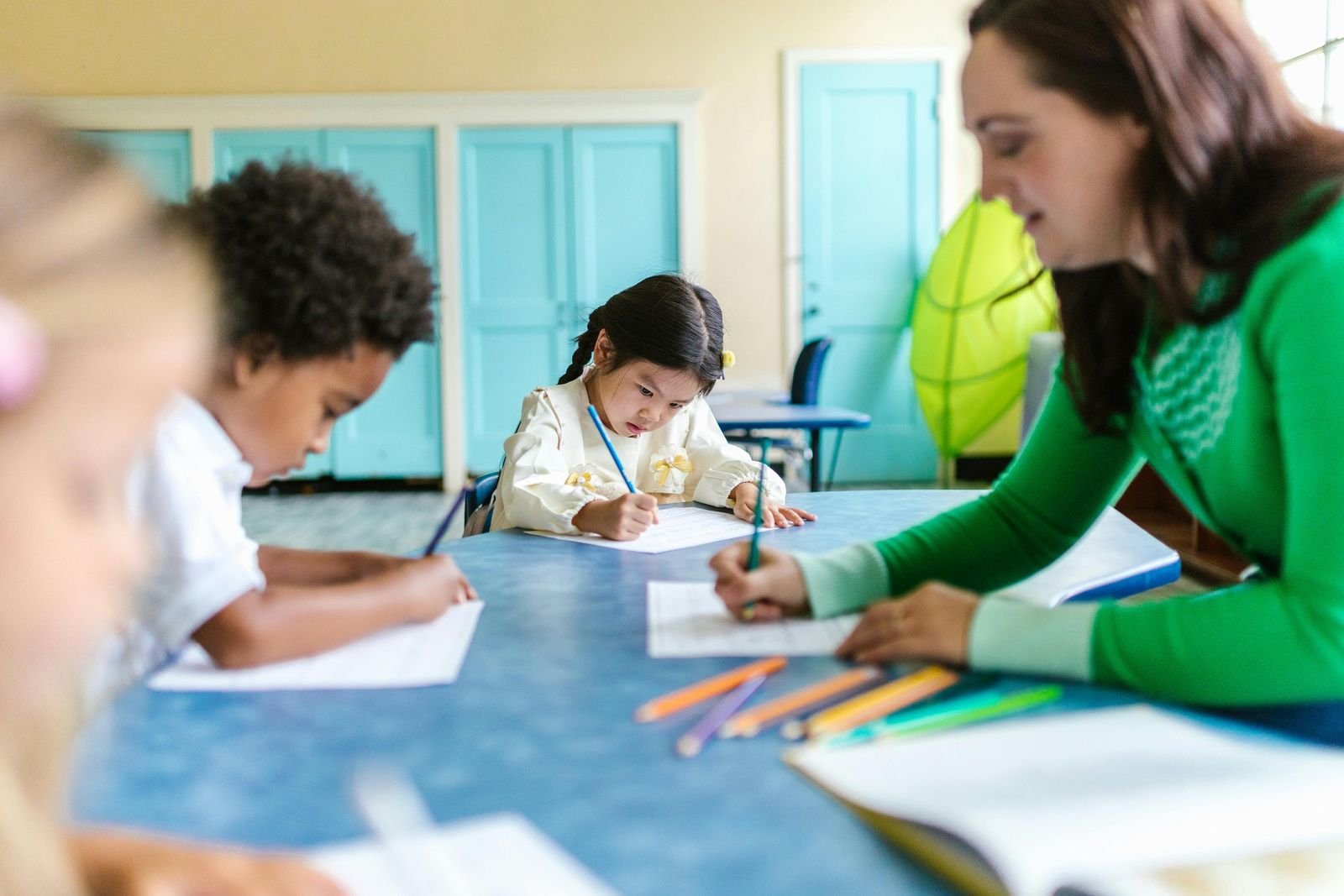 Professora acompanhando crianças da educação infantil em uma atividade de escrita